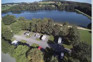 Campingplatz am See mit Stellplätzen, Zelten und Wohnwagen, umgeben von Wiesen und Bäumen, Blick von oben.