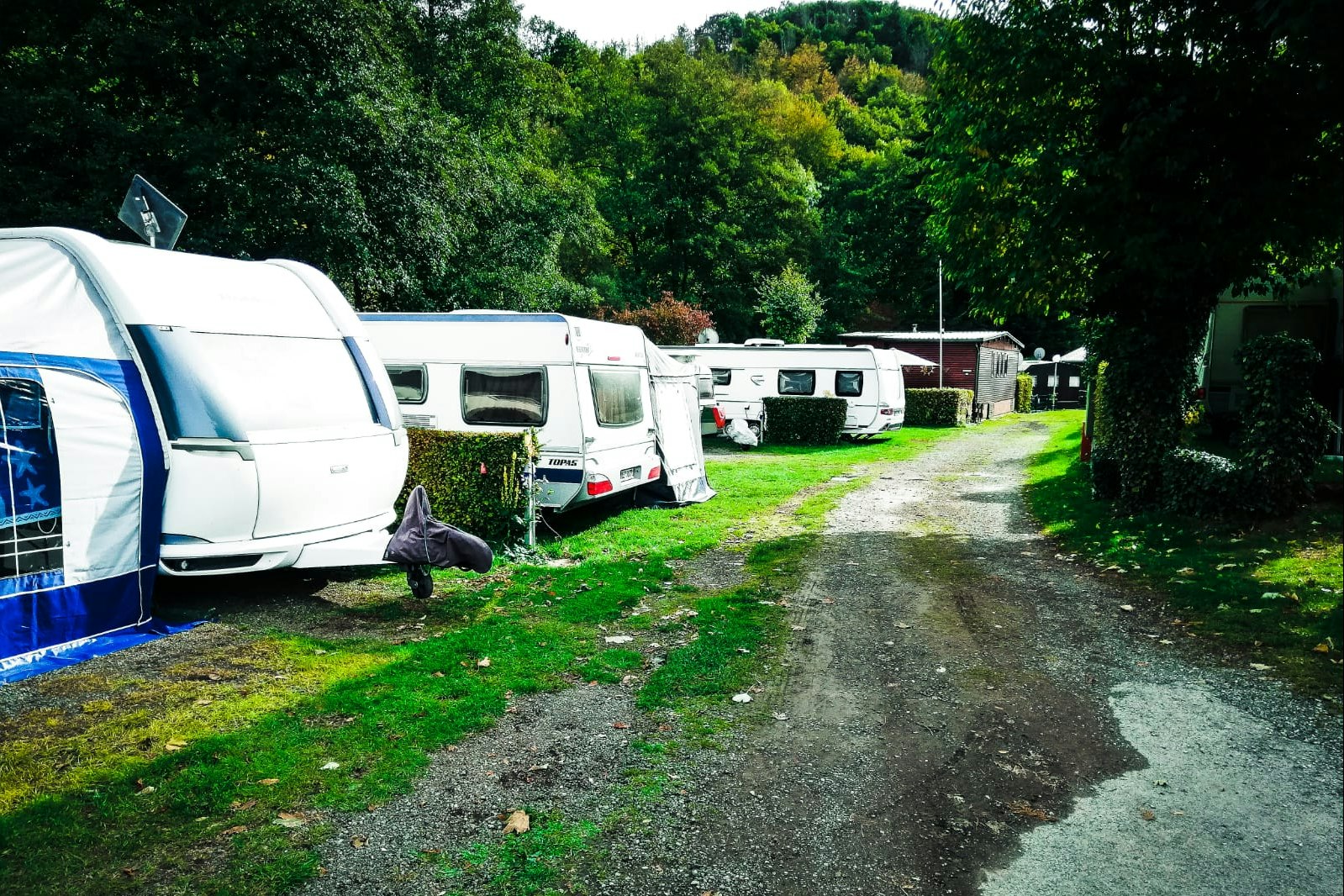 Wohnwagen und Wohnmobil auf einem Campingplatz, mit Hecken, Rasen und Kiesweg zwischen den Stellplätzen.