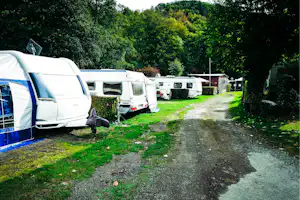 Wohnwagen und Wohnmobil auf einem Campingplatz, mit Hecken, Rasen und Kiesweg zwischen den Stellplätzen.