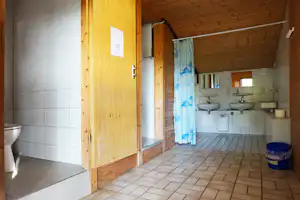Badezimmer im Campingbereich mit Waschbecken, Fliesenboden und offenen Türen, im Hintergrund weitere Spülbecken und Ablageflächen.