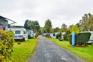 Campingplatz-Gartenweg mit Wohnmobilen und Mobilheimen, Hecken und Rasenflächen entlang der Straße.