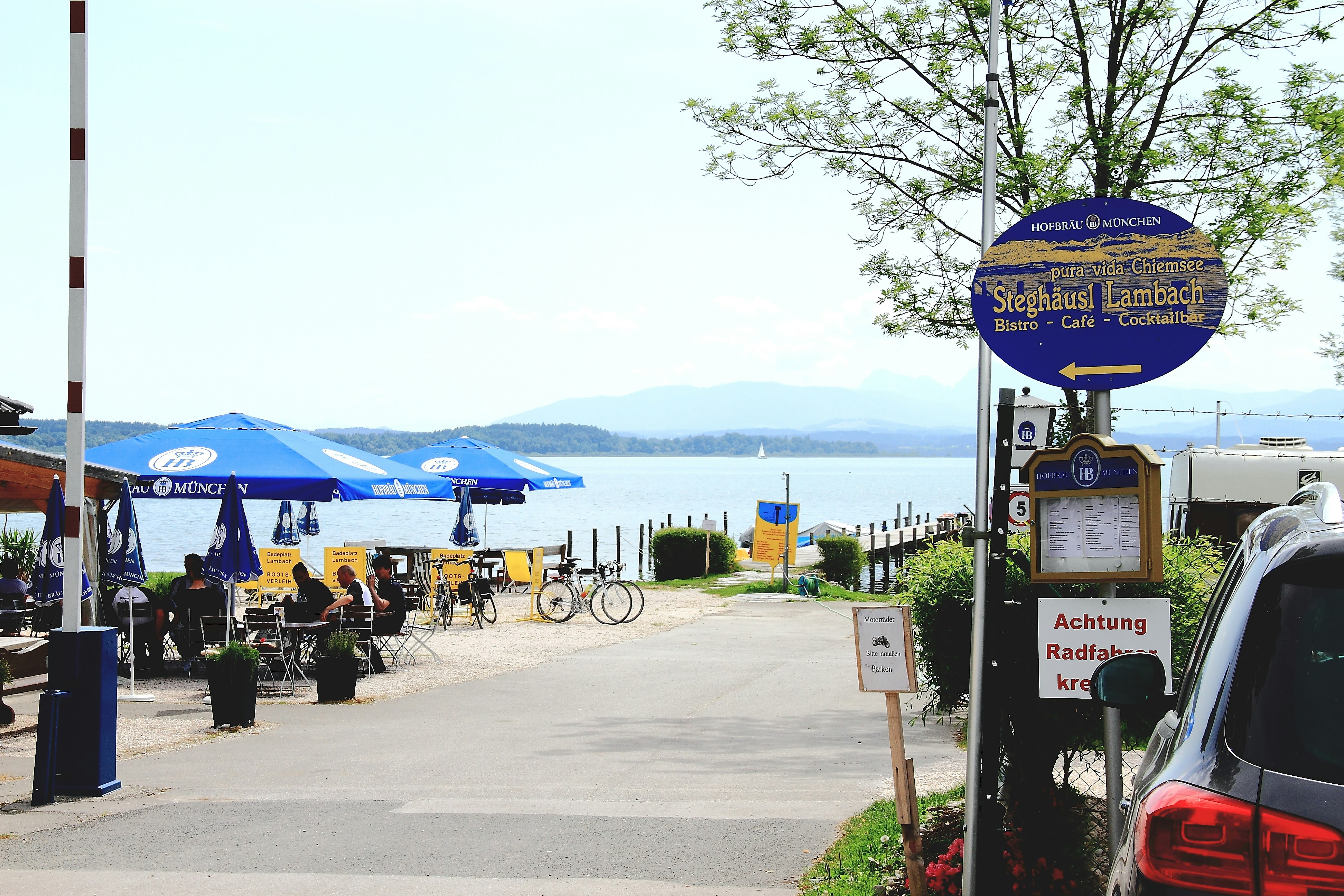 Chiemsee Camping Lambach  -  Einfahrt vom Campingplatz mit Terrasse vom Restaurant am See