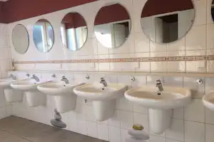 Reihe weißer Waschbecken im Camping-Badezimmer, große Spiegel über den Becken und Fliesenboden in hellen Farben.