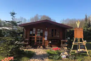 Holzhütte auf dem Campingplatz mit Terrasse, Gartenweg, Blumenbeeten und Staffelei im Vordergrund.