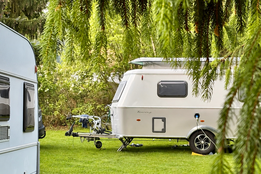 Wohnwagen auf einem Campingplatz im Grünen, neben einem weiteren Caravan; Rasenfläche und Bäume im Hintergrund.
