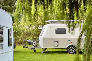 Wohnwagen auf einem Campingplatz im Grünen, neben einem weiteren Caravan; Rasenfläche und Bäume im Hintergrund.