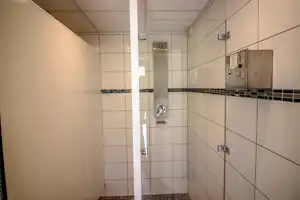 Duschkabine mit Fliesenwand, Duschkopf und Armaturen in einem hellen Sanitärbereich.