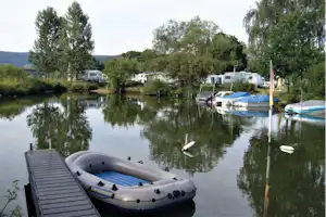 Boot auf dem Steg am ruhigen Campingsee, im Hintergrund Wohnwagen und Stellplätze mit Bäumen und Wasserfläche.