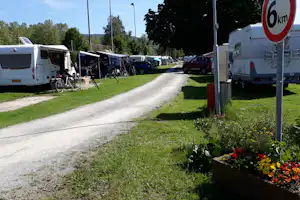 Wohnmobile auf einem Campingplatz, dazwischen ein Kiesweg und Stellplätze mit Sitzgelegenheiten, im Hintergrund Bäume und Fahrzeuge.