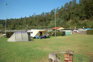Campingzelt auf einer Wiese, daneben Wohnwagen und Wohnmobil, im Hintergrund Hecken und hohe Bäume.