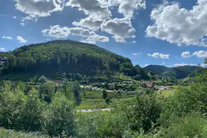 Blick ins Tal mit bewaldeten Hügeln und Bergen, Campingplatz im Grünen mit Wegen und kleinen Gebäuden in der Ferne.