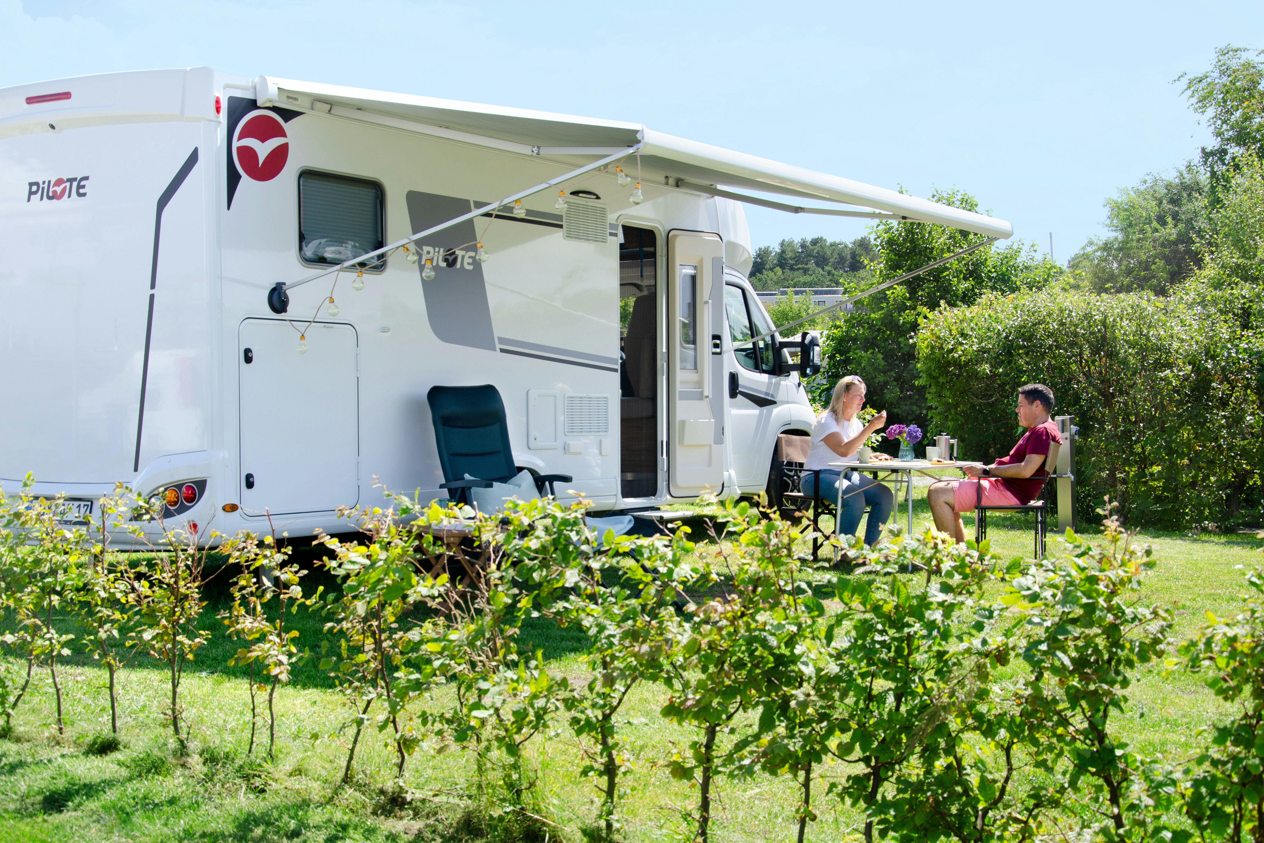 Campingplatz Muschelgrund - Camper sitzen an einem Tisch vor ihrem Wohnmobil auf einem Standplatz