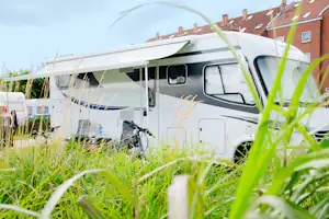 Wohnmobil auf dem Campingplatz mit Vorzelt, im Vordergrund grünes Gras und im Hintergrund rote Backsteinhäuser.