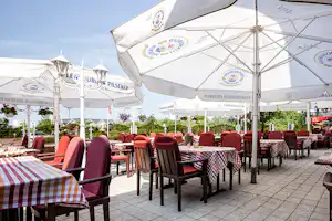Terrasse mit vielen Stühlen und Tischen unter weißen Zelten, mit gestreiften Tischdecken und Blick auf weitere Zelte.