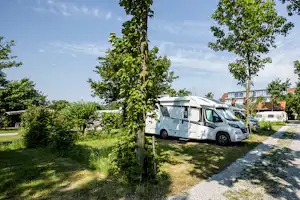 Wohnmobil auf einem Stellplatz im Grünen, daneben weitere Camper und ein Weg zwischen Bäumen und Hecken.