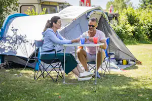 Campingzelt im Garten, zwei Personen sitzen am Tisch mit Getränken und Campingstühlen vor dem Zelt.