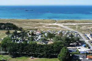 Campingplatz an der Küste mit Wohnwagen, Bäumen und Straße zum Meer, Blick auf türkisfarbenes Wasser und Inseln.