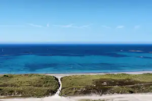 Blick von den Dünen auf einen Strand und das Meer mit Inseln am Horizont.