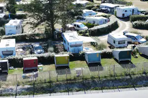 Wohnmobile und Campingbusse auf einem Campingplatz zwischen Hecken und Bäumen, mit Schotterwegen und Stellplätzen.