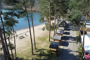 Campingplatz am See mit Stellplätzen, Tischen und Bänken im Schatten der Bäume, Blick auf das Wasser.