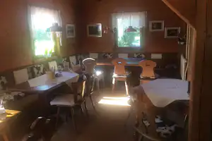 Gemütlicher Essbereich in einer Holzunterkunft mit Tisch, Stühlen, Lampen und Fenstern zur grünen Umgebung.