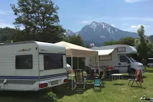 Wohnwagen und Vorzelt auf einem Campingplatz, mit Gartenmöbeln und Bergblick im Hintergrund.