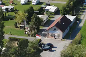 Luftaufnahme eines Campingplatzes mit Wohnwagen, kleinen Häusern und einem großen Gebäude, umgeben von Bäumen und Wegen.
