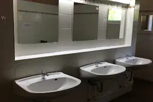 Camping-Badezimmer mit mehreren Waschbecken, Armaturen und Fliesenwand, dahinter Fenster mit Blick ins Grüne.