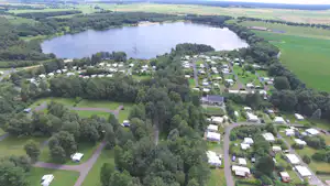 Luftaufnahme eines Campingplatzes am See mit vielen Wohnmobilen, Wegen, Bäumen und einem großen Gewässer im Hintergrund.