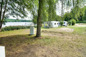 Stellplätze am See mit Rasenfläche, Bäumen und mehreren Wohnmobilen sowie Mobilheimen am Uferweg.