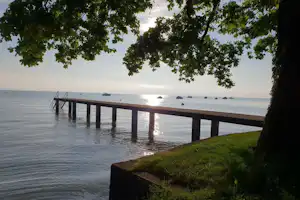 Holzsteg am See mit Blick auf das Wasser, Bojen und Boote, eingerahmt von Bäumen am Ufer.