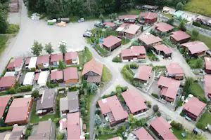 Luftaufnahme einer Campinganlage mit mehreren Ferienhäusern und roten Dächern, Wegen, Rasenflächen und parkenden Autos.