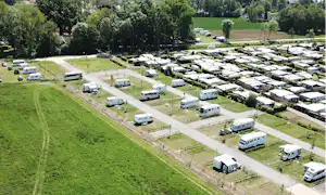 Luftaufnahme eines Campingplatzes mit vielen Stellplätzen, Wohnmobilen und Wohnwagen entlang breiter Wege und grüner Wiesen.