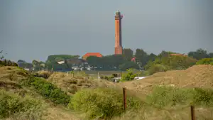 Kirchturm in der Ferne über grünen Hügeln, im Hintergrund Häuser und ein Campingplatz am Wegesrand.