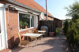 Terrasse am Ziegelhaus mit Tisch und Stühlen, Schiebetür, Pflanzkübeln und Zaun im Campingbereich.