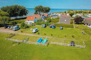 Luftaufnahme von Campinghäusern und Wohnwagen auf einer grünen Anlage, mit Rasenflächen, Wegen, Hecken und Blick auf das Meer.
