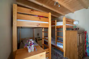 Holz-Etagenbett in einem Campinghaus mit mehreren Betten, Schrank, Tisch und Blumenstrauß auf dem Tisch.