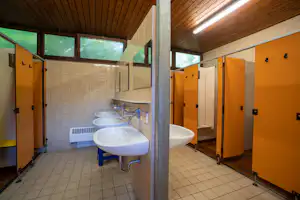 Camping-Badezimmer mit Waschbecken, Armaturen und orangefarbenen Spinden, Fliesenboden und Holzdecke mit Lichtleisten.