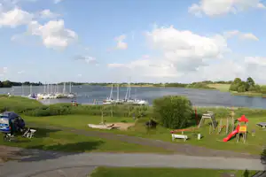 Campingplatz Wees - Kinderspielplatz auf dem Campingplatz mit Rutsche, Klettergerüst und Wippe mit Wasser des Ostseefjords im Hintergrund