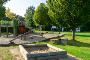Spielplatz auf dem Campingplatz: Sandkasten, Rutsche und Klettergerüst im Grünen mit Bäumen und Stellplätzen im Hintergrund.