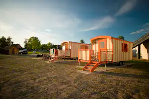 Orangefarbene Mobilheime mit Veranda und Stufen auf einem Campingplatz, daneben ein Fahrrad und ein weiterer Wohnwagen.