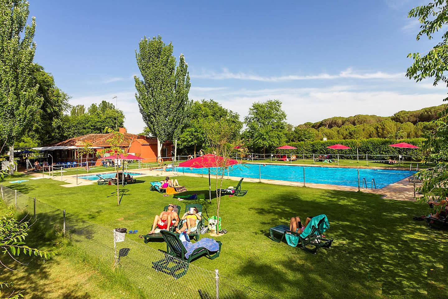 Campingred El Astral  -  Camper am Pool vom Campingplatz mit Sonnenschirmen und Liegestühlen auf grüner Wiese
