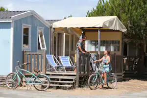 Blauer Camping-Wohnwagen mit Veranda, zwei Fahrrädern davor und zwei Personen am Eingang.
