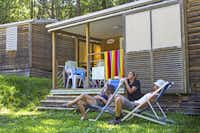 Campéole Le Lac  -  Camper in Liegestühlen auf grüner Wiese am Mobilheim vom Campingplatz mit Veranda