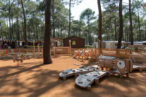 Holzterrasse mit Sitz- und Liegestühlen, daneben ein Fasssauna-ähnliches Holzfass, umgeben von Kiefern im Campingbereich.