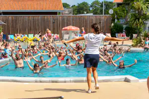 Eine Person steht am Beckenrand und hält die Arme aus, während viele Kinder im Pool planschen.