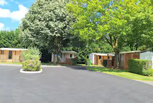 Reihen von Bungalows und kleinen Gebäuden am Campingplatz entlang einer asphaltierten Straße, umgeben von Bäumen und Grün.