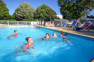 Familie im blauen Schwimmbecken eines Campingplatzes, im Hintergrund Liegestühle und Bäume, klare Umrandung am Beckenrand.