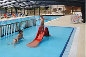 Schwimmbecken mit Rutsche im Camping-Paradis, daneben Liegen und ein überdachter Bereich mit Glasdach.
