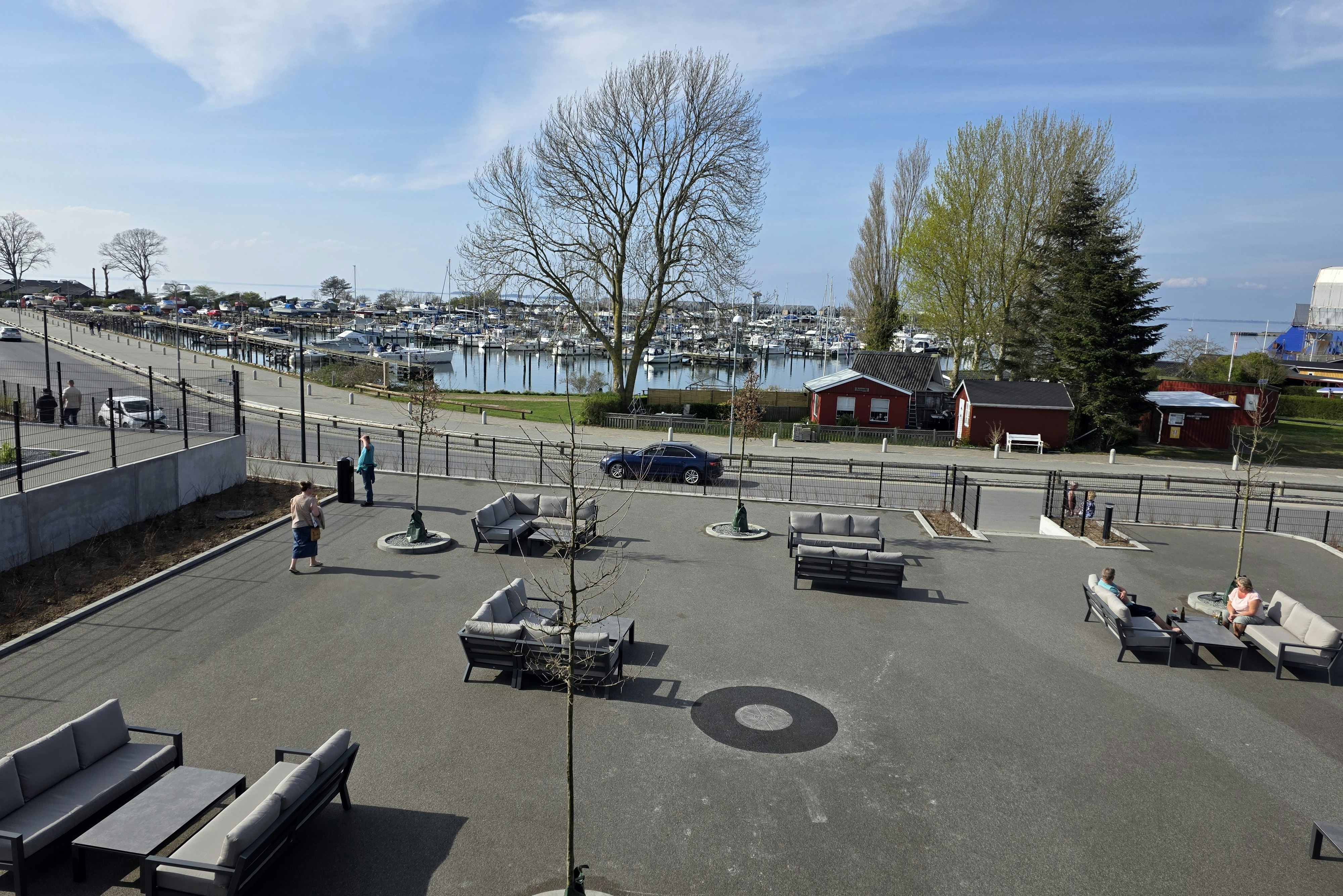 Terrasse am Campingplatz mit Sitzmöbeln, Blick auf den Hafen und viele Boote an den Stegen.